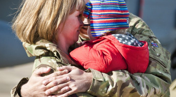 A Royal Air Force serviceman with IX(B) Squadron hugs his wife and child after returning from Afghanistan.