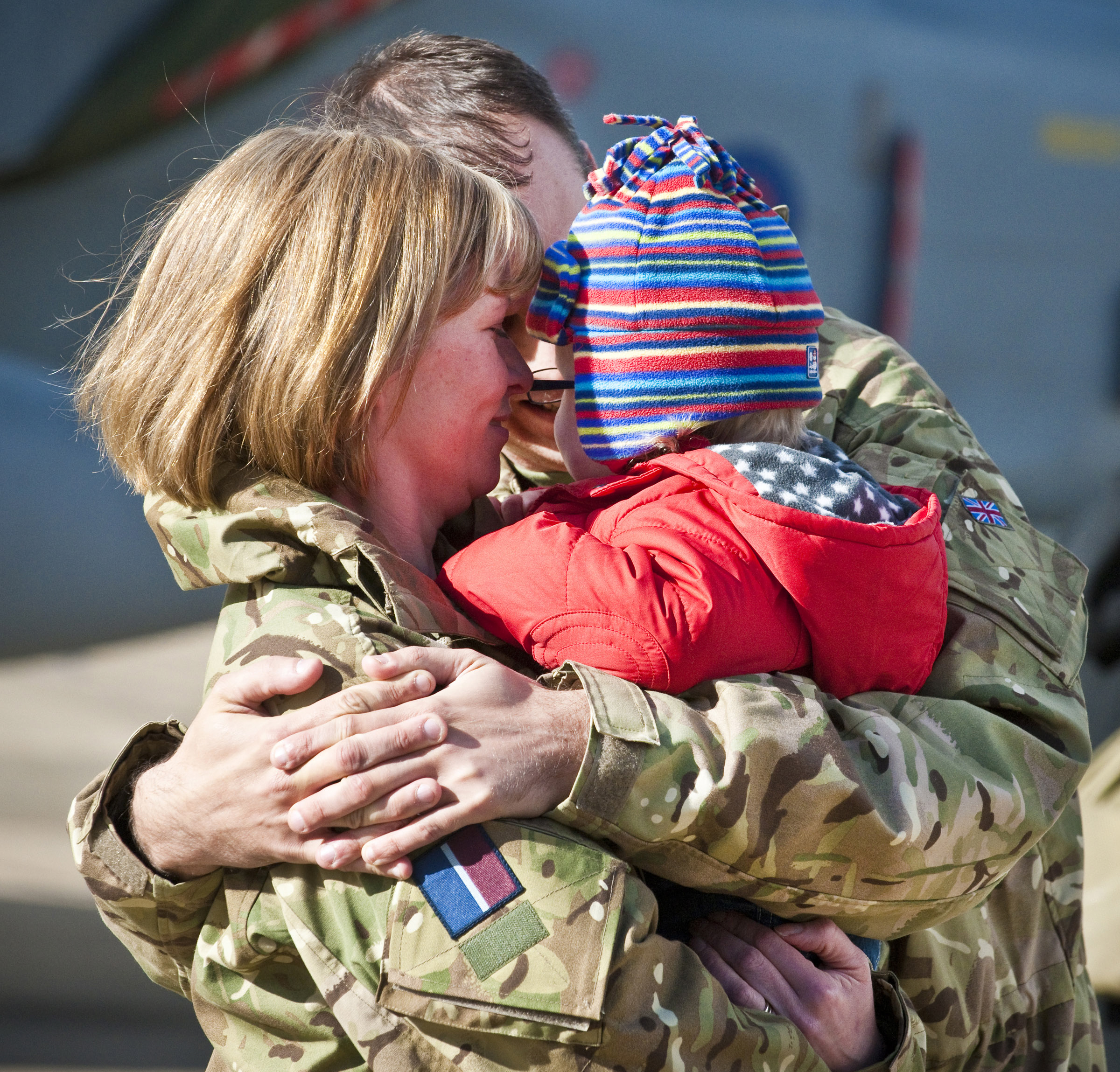 A Royal Air Force serviceman with IX(B) Squadron hugs his wife and child after returning from Afghanistan.