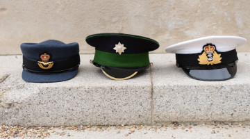 Left to right Royal Air Force, British Army and Royal Navy caps sitting in a row on a step