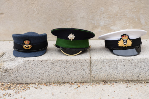 Left to right Royal Air Force, British Army and Royal Navy caps sitting in a row on a step