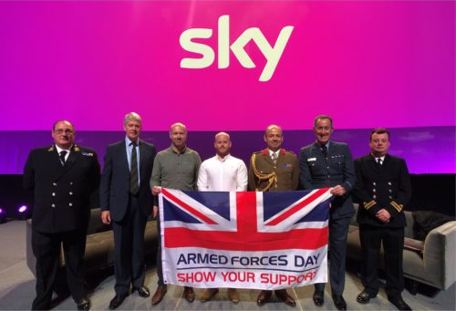 Sky employees smiling at the camera holding a Armed Forces Day flag. 
