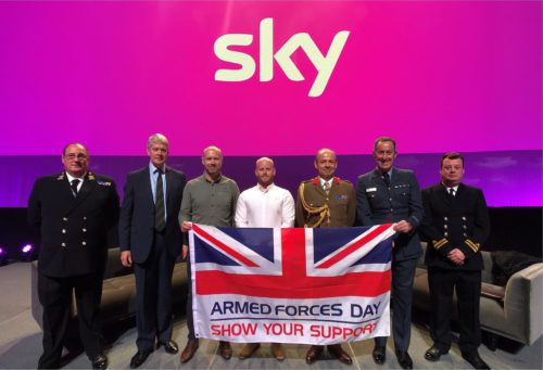 Sky employees smiling at the camera holding a Armed Forces Day flag.